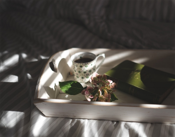 A book, a cup of coffee and a cluster of hydrangea flowers on a wooden tray